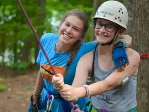 a couple of women wearing helmets and harnesses holding a bow and arrow