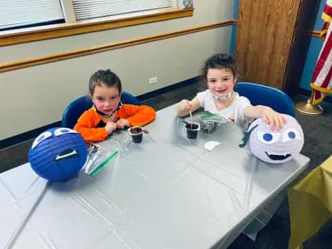 a couple of kids sitting at a table with a game controller