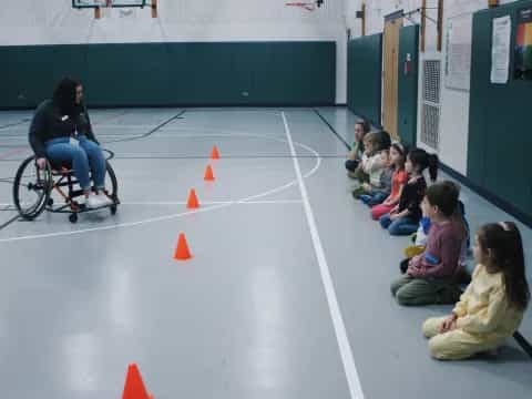 a person in a wheelchair in a gym with children