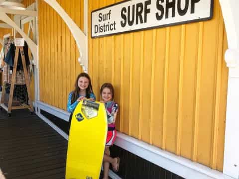 girls holding surfboards in front of a yellow building