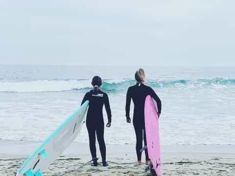 a couple of people stand on a beach with surfboards