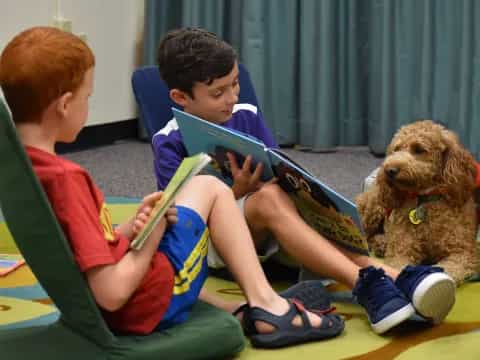 a couple of boys sitting on the floor reading a book to a dog