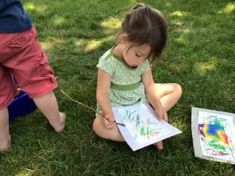 a young girl sitting on the grass writing on a book