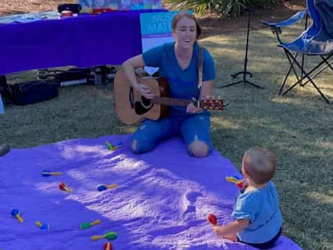 a person playing guitar next to a baby on a blanket