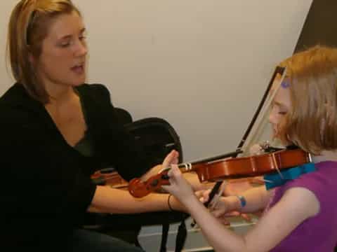 a woman playing a violin to a young girl