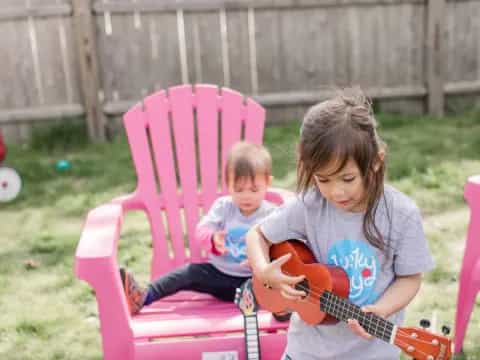a person playing a guitar next to a baby sitting in a pink chair