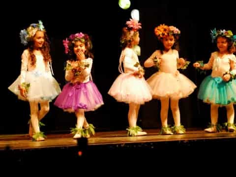 a group of girls wearing dresses and flowers on a stage