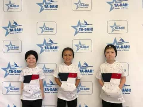 a group of girls in matching white shirts standing in front of a white wall with blue writing