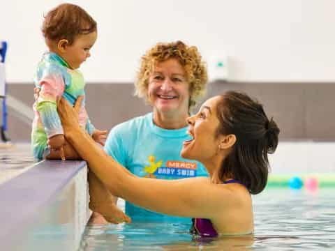 a man and woman holding a baby in a pool