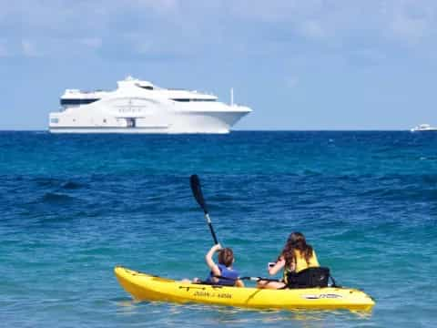 a couple of people in a yellow kayak in the water with a cruise ship in the background