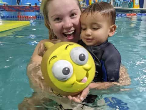 a person and a baby in a pool with a yellow toy in it