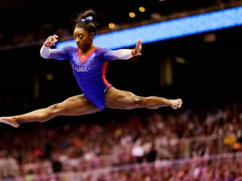 a person in a leotard jumping in the air in front of a crowd