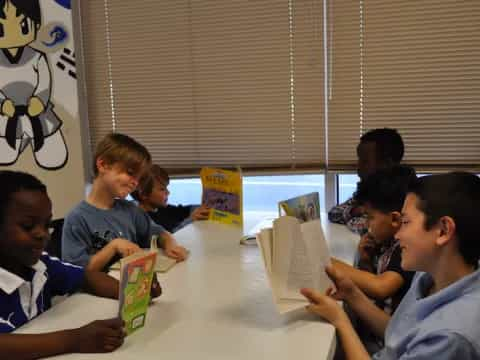 a group of children sitting at a table reading books