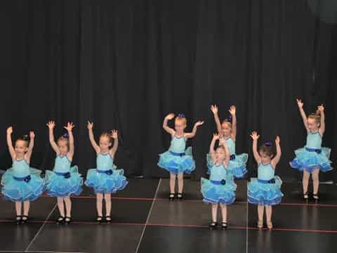 a group of girls in blue dresses dancing on a stage