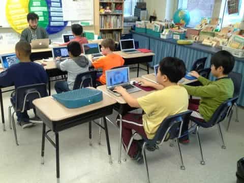 a group of kids sitting at desks using laptops