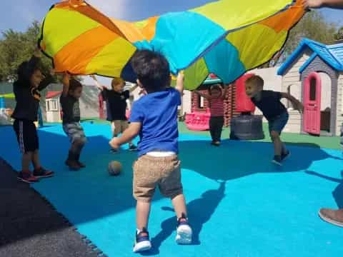 a group of kids playing with a large yellow and blue umbrella