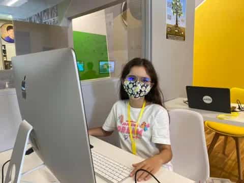 a person sitting at a desk with a computer and a mask on the face