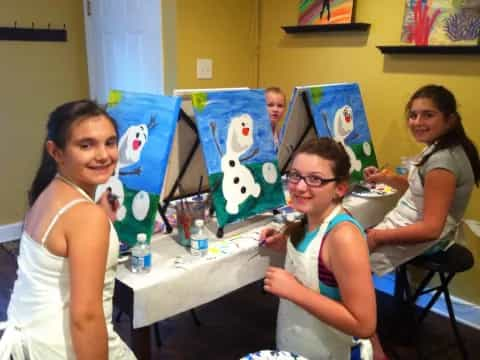 a group of girls sitting at a table with a painting on the wall