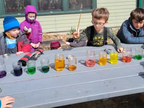 a group of kids sitting at a table with cups of liquid