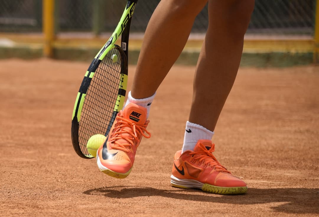 person in red nike shoes holding tennis racket