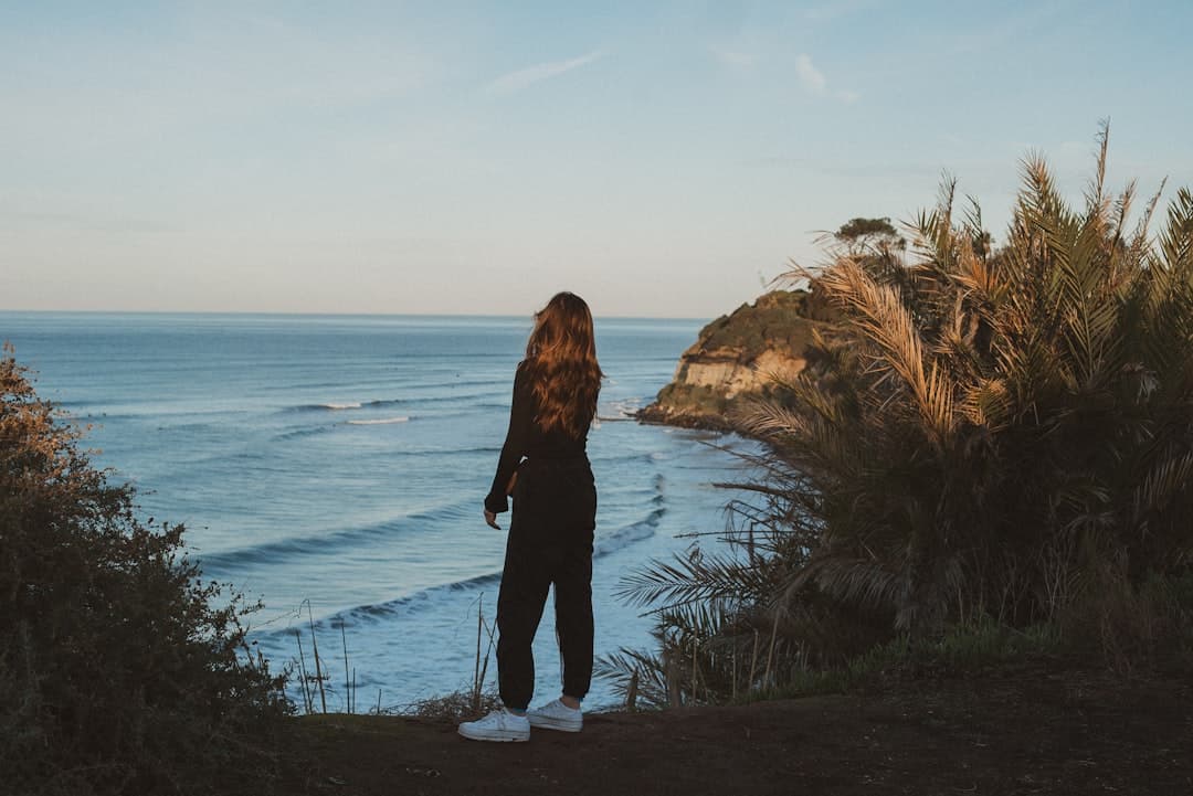 woman in black jacket standing on brown rock near body of water during daytime