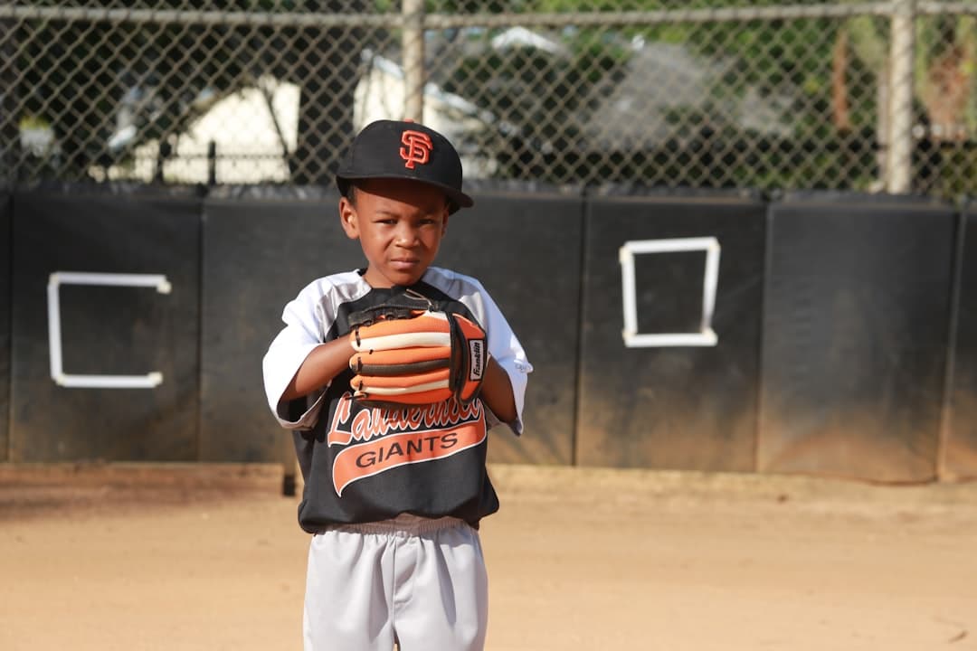 boy in orange and black jacket and white pants standing on field during daytime