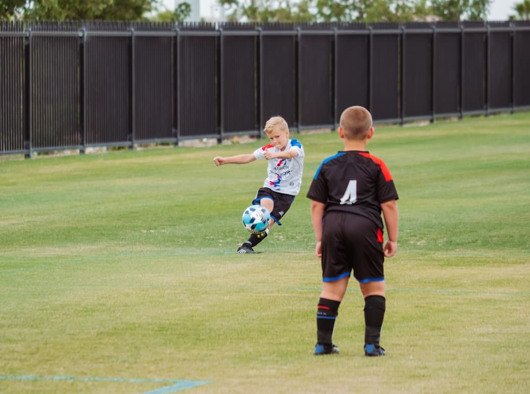 2 boys playing soccer on green grass field during daytime