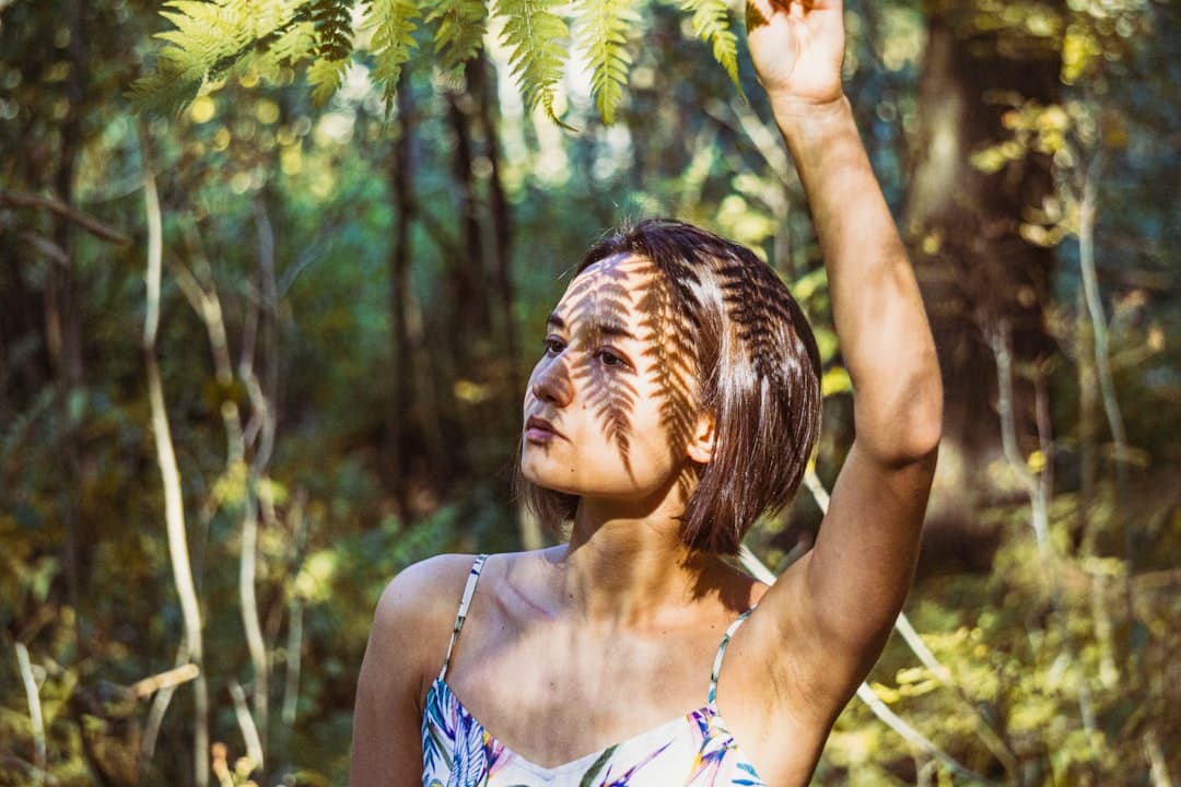 woman in blue and white floral spaghetti strap top standing near green trees during daytime