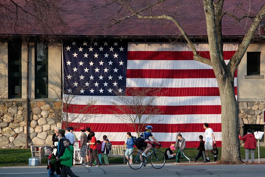 a group of people riding bikes past a large american flag