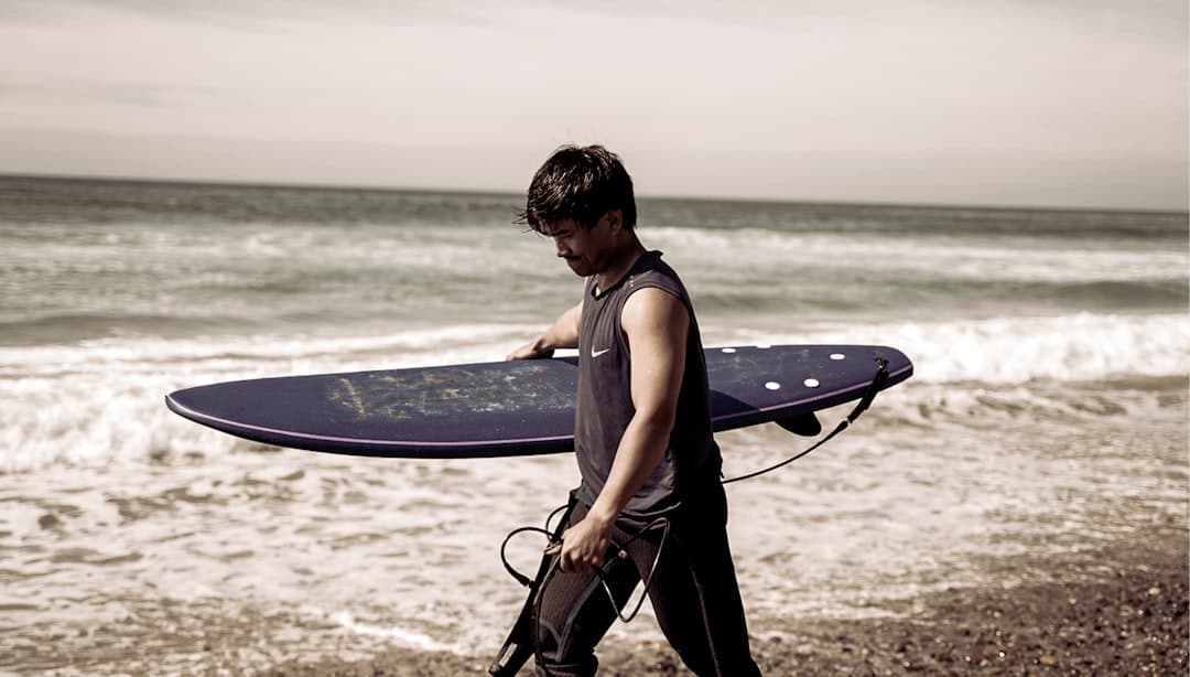 a young man carrying a surfboard on a beach