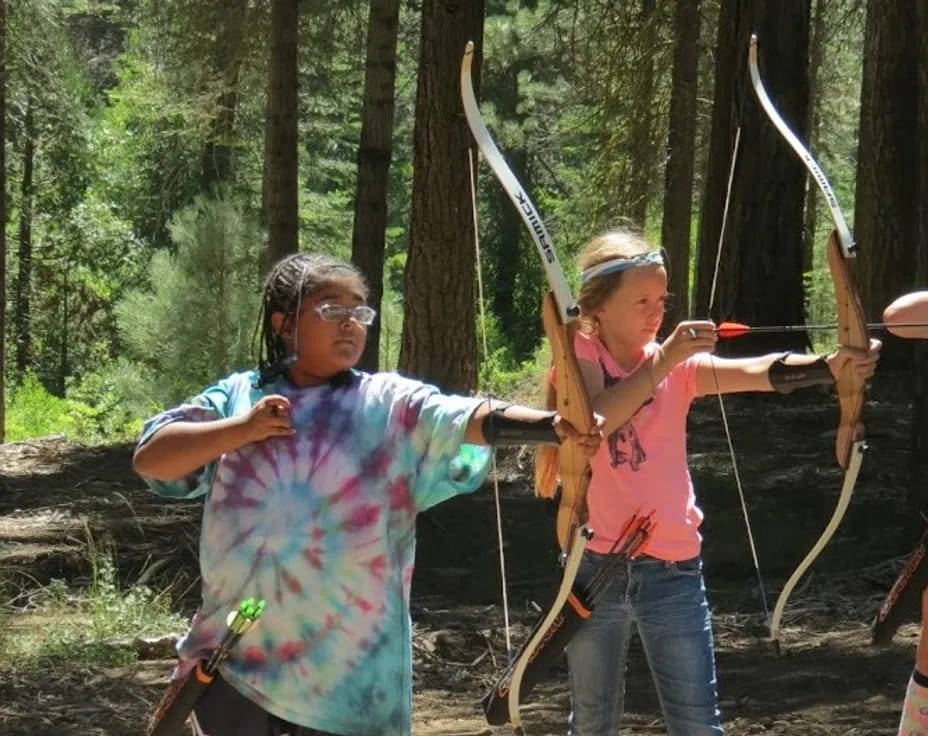 a person and a girl holding bows and arrows in the woods