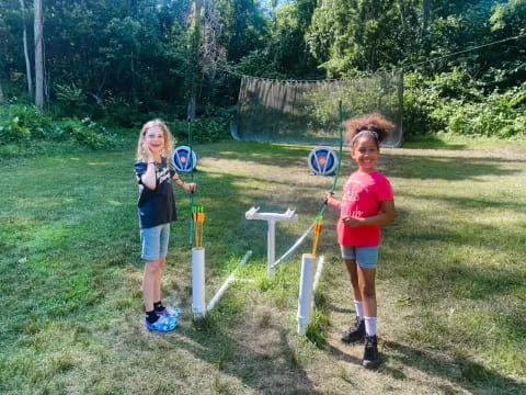 a couple of girls playing with bows and arrows in a yard