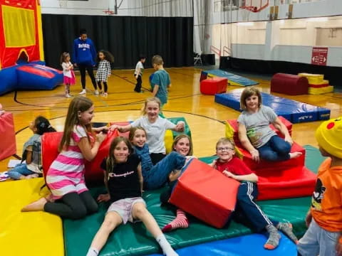 a group of children sitting on a mat in a gym