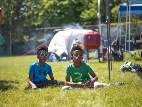 a couple of boys sitting on the grass with a tent in the background