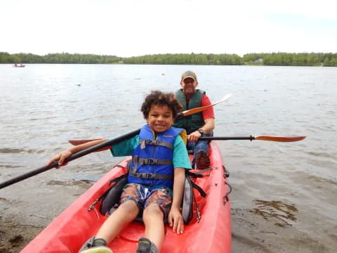 a boy in a red kayak with a person in the background