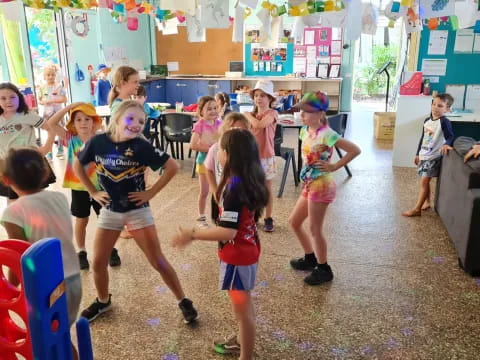 a group of children dancing in a room with colorful chairs and tables