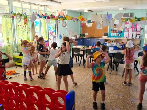 a group of children dancing in a room with red and blue chairs