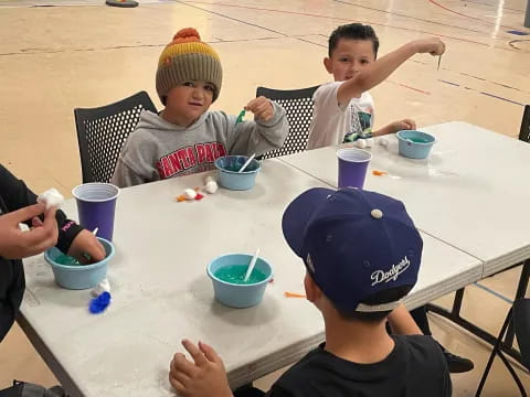 a group of kids sitting at a table with blue cups and a blue hat