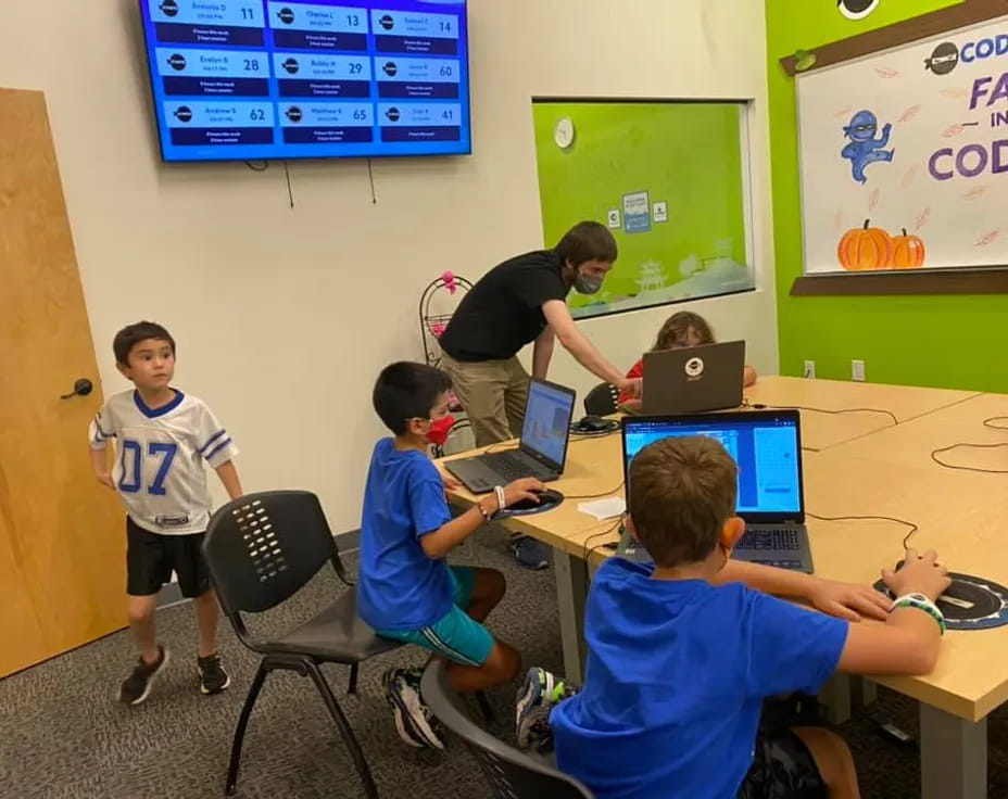 a group of kids sitting at a table with laptops