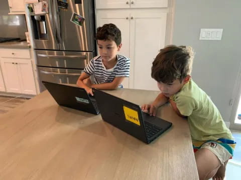 a couple of boys looking at a laptop on a table