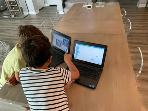 a couple of people sit at a table with laptops