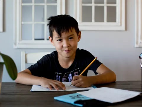 a boy sitting at a table writing on a piece of paper