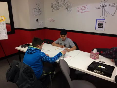 a couple of men sitting at a table with a laptop and a backpack