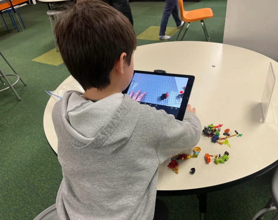 a boy sitting at a table with a tablet and toys on it
