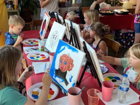 a group of children sitting at a table painting