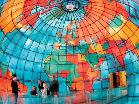a group of people standing in a room with a colorful ceiling with Mapparium in the background