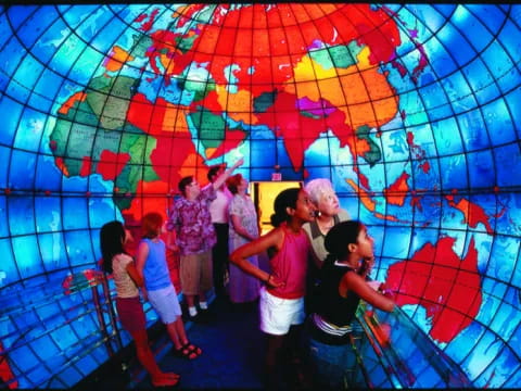 a group of people standing in front of a wall with colorful glass with Mapparium in the background