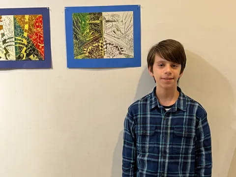 a boy standing in front of a wall with paintings on it