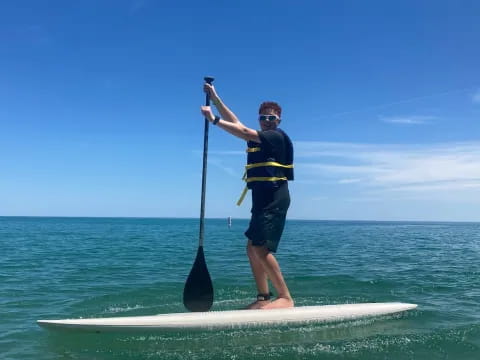 a man on a paddle board holding a pole and a fishing pole