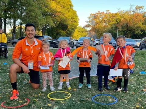 a group of children wearing orange vests and standing on grass